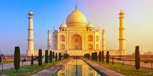 The majestic Taj Mahal glowing in soft orange and pink hues during a peaceful morning sunrise in Agra, India.