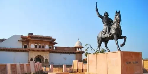 A bronze statue of the valiant Maharaja Suraj Mal, the 18th-century founder of Bharatpur, standing prominently against a clear sky.