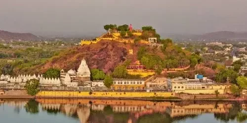 The magnificent architecture of Badal Mahal built from traditional pareva stone, reflecting in the tranquil waters of Gaib Sagar Lake at dusk in Dungarpur, Rajasthan.